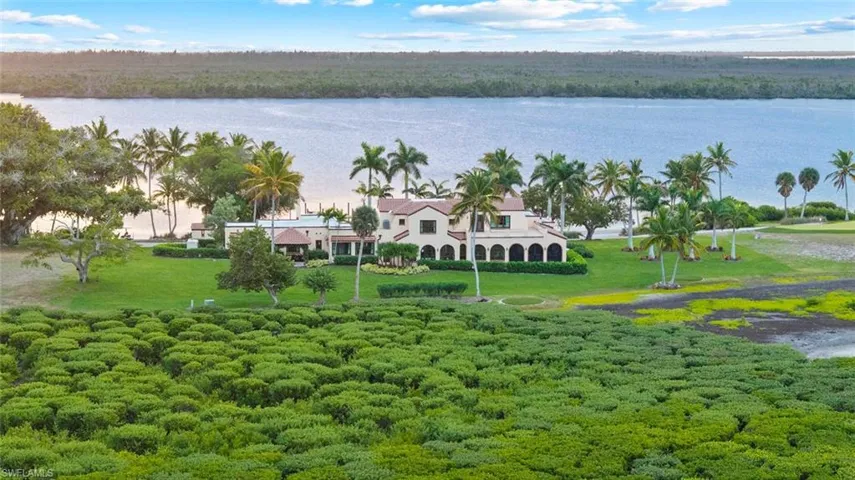 MAIN HOUSE - The property features a multi-story residence with arched windows and a tile roof, situated on a large grassy expanse with palm trees