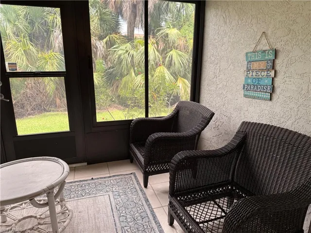 Screened enclosure featuring a tile floor, textured wall finish, and exterior views of tropical foliage