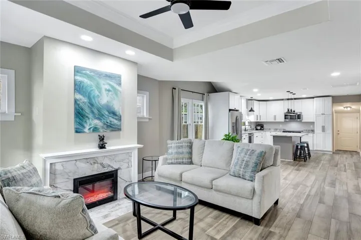 Living room featuring recessed lighting, light wood-type flooring, ornamental molding, a high end fireplace, and a raised ceiling