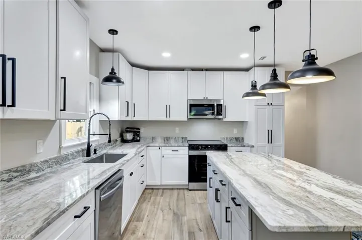 Kitchen featuring light stone countertops, stainless steel appliances, decorative light fixtures, a center island, and recessed lighting