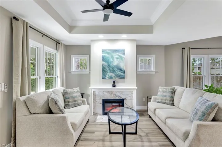 Living room featuring wood finished floors, a tray ceiling, ornamental molding, ceiling fan, and recessed lighting