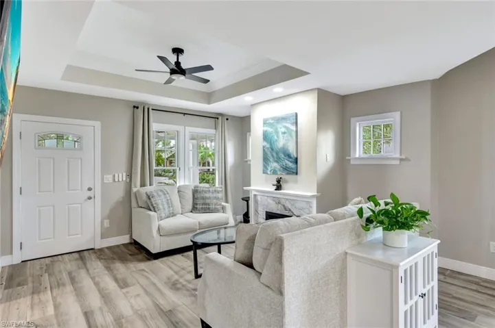 Living room with a raised ceiling, light wood finished floors, healthy amount of natural light, a high end fireplace, and recessed lighting