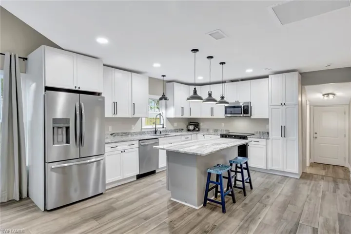 Kitchen featuring stainless steel appliances, a kitchen bar, hanging light fixtures, light stone countertops, and white cabinets
