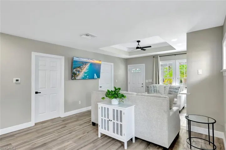 Living area with a tray ceiling, light wood-style flooring, and ceiling fan