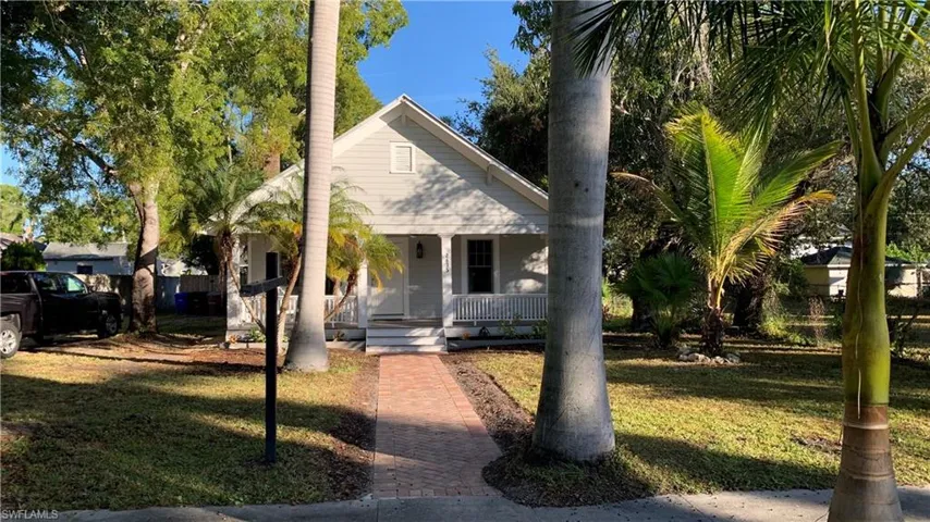 Bungalow with mature royal palms, red brick walkway leading to covered porch