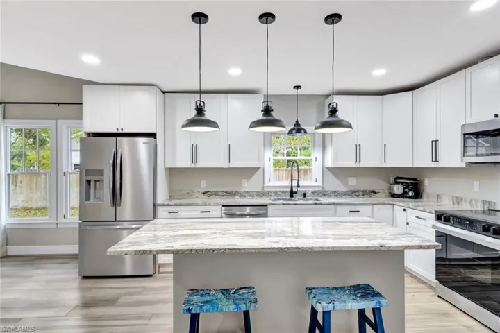 Kitchen with stainless steel appliances, a kitchen breakfast bar, light stone counters, white cabinets, and recessed lighting