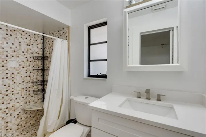 Bathroom featuring a tiled shower with a built-in seat, a white vanity with an integrated sink, a rectangular framed mirror, and a fixed window