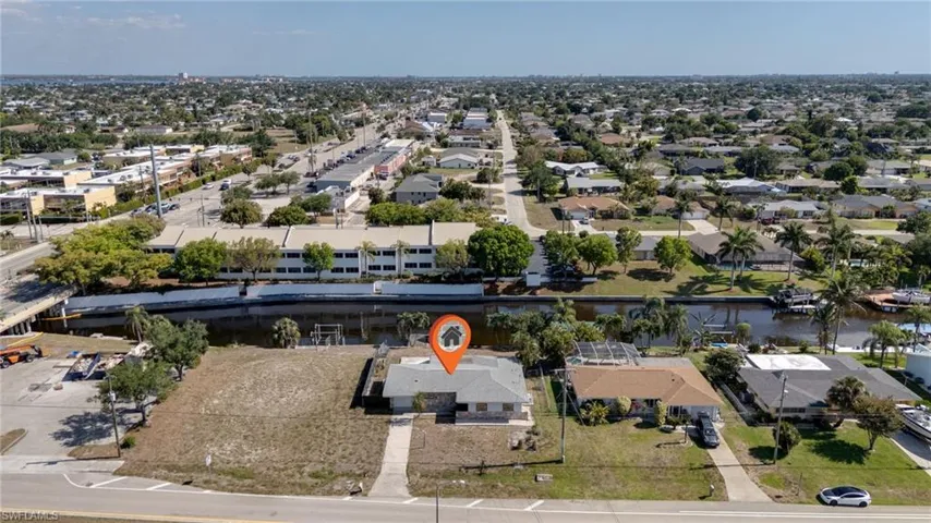 Aerial view of a residential property featuring a single-story structure with a gray roof and concrete driveways, situated on a lot with undeveloped green space