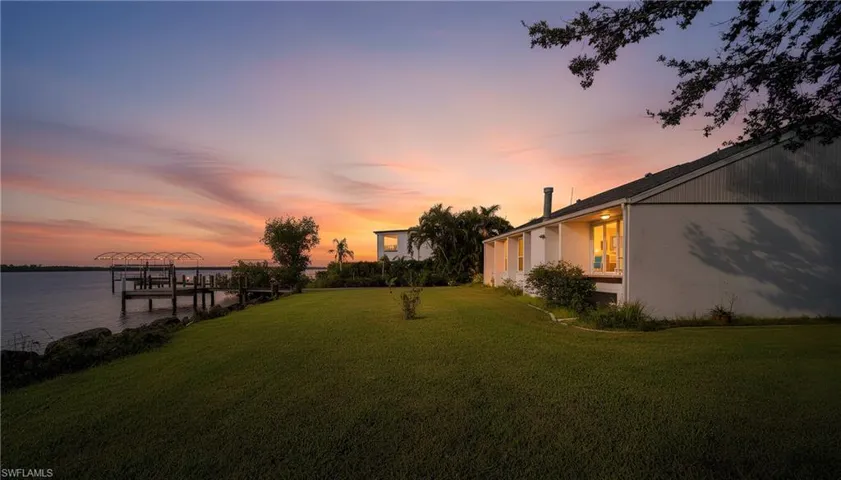 Yard at dusk featuring boat lift, a water view, a yard, and a boat dock