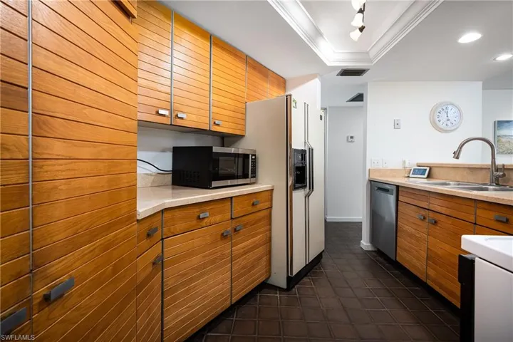 Kitchen with ornamental molding, brown cabinetry, light countertops, stainless steel appliances, and a tray ceiling
