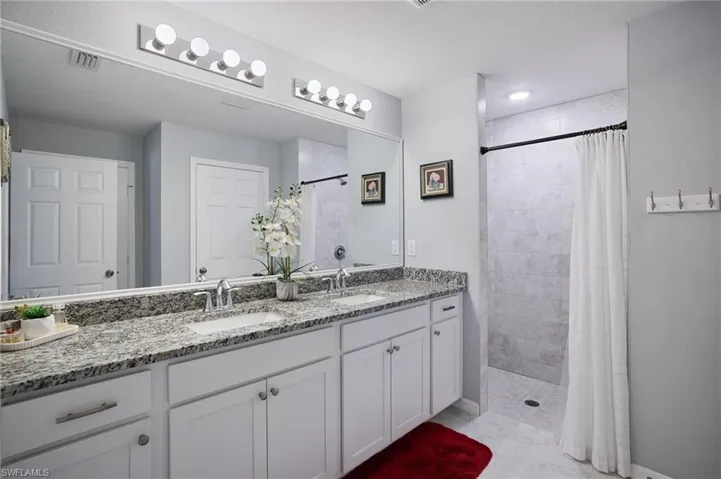 Primary bathroom featuring double vanity and tiled walk in shower with curtain