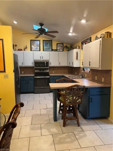 Kitchen with vaulted ceiling, a ceiling fan, refrigerator, range, and white cabinets