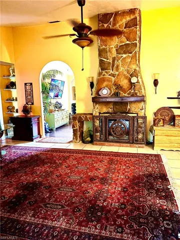 featuring a stone fireplace, ceiling fan, and tile patterned flooring