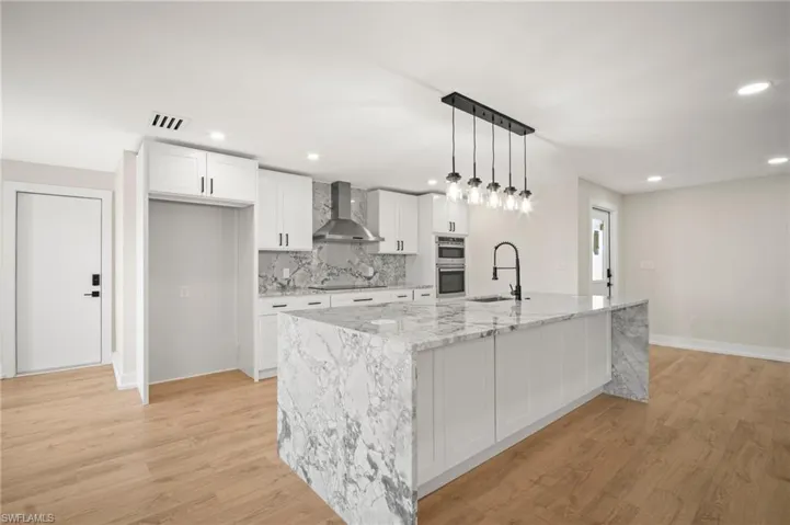 Kitchen featuring visible vents, wall chimney range hood, black electric cooktop, white cabinets, and a large island with sink