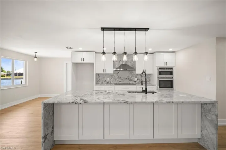 Kitchen featuring baseboards, stainless steel double oven, wall chimney exhaust hood, and white cabinets
