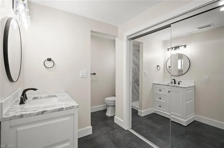 Full bath with toilet, baseboards, visible vents, a sink, and two vanities