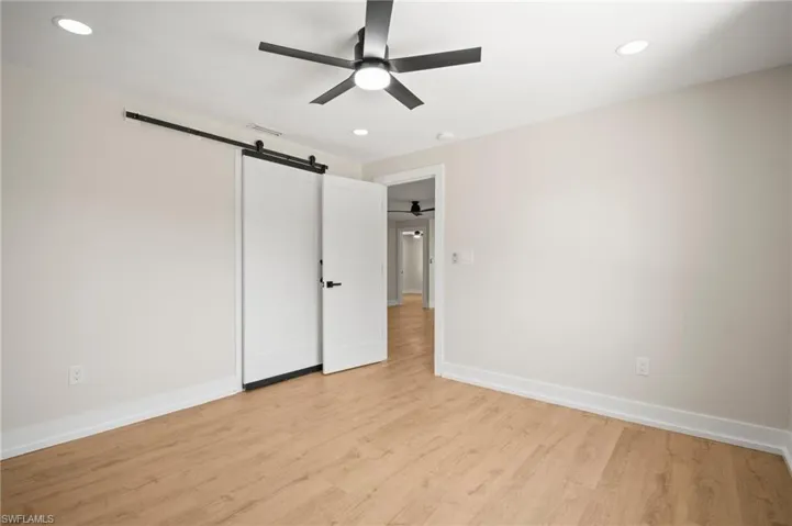 Unfurnished bedroom featuring a barn door, visible vents, recessed lighting, light wood-style flooring, and baseboards