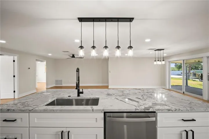 Kitchen featuring white cabinetry, a sink, open floor plan, and stainless steel dishwasher