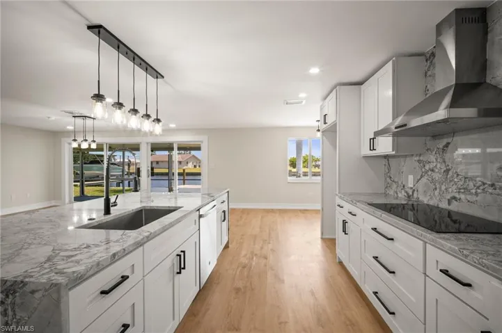 Kitchen with dishwasher, light wood finished floors, a sink, wall chimney range hood, and black electric cooktop