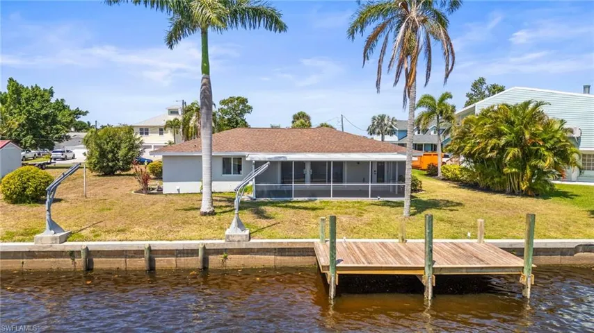 Back of property with a sunroom, a water view, and a lawn