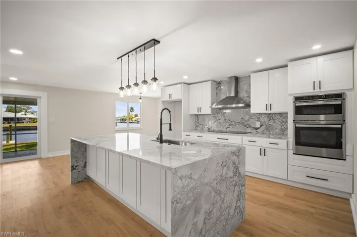 Kitchen with light wood-style floors, a sink, wall chimney exhaust hood, and tasteful backsplash