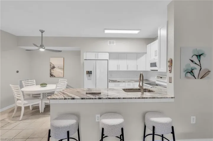 Kitchen with white appliances, backsplash, sink, a kitchen bar, and white cabinetry