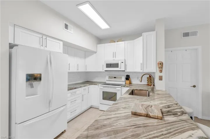Kitchen featuring tasteful backsplash, white appliances, sink, light tile patterned floors, and white cabinets