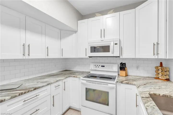 Kitchen with white appliances, light stone countertops, light tile patterned floors, tasteful backsplash, and white cabinetry
