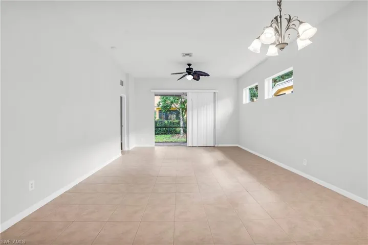 Tiled empty room featuring ceiling fan with notable chandelier and plenty of natural light