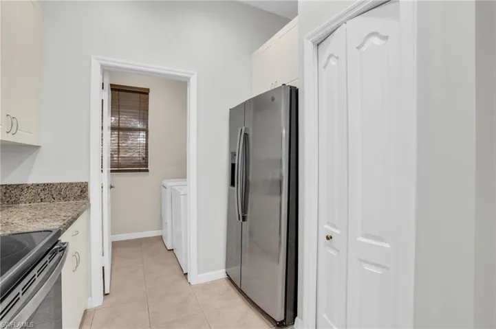 Kitchen with range, light stone counters, light tile patterned floors, stainless steel refrigerator with ice dispenser, and white cabinetry