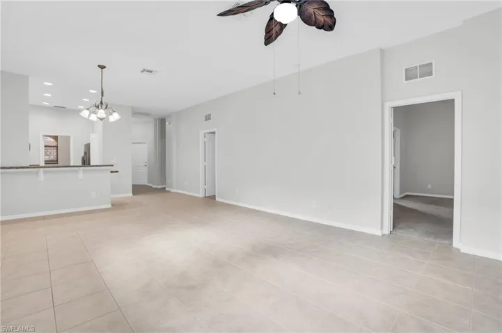 Unfurnished living room with light tile patterned flooring and ceiling fan with notable chandelier