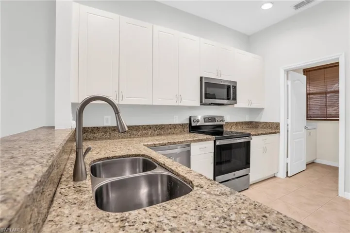 Kitchen featuring light tile patterned flooring, appliances with stainless steel finishes, light stone counters, and white cabinetry