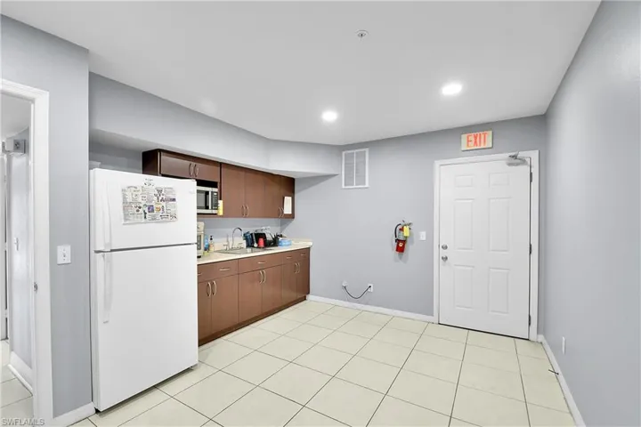 Kitchenette featuring wood-finish cabinetry, a stainless steel sink, and light-toned tile flooring