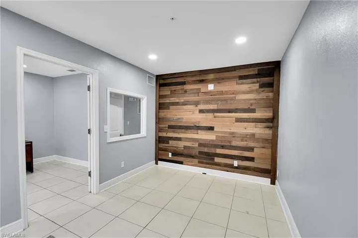 Accent wall featuring varied wood-finish planks, recessed ceiling lighting, and light tile flooring
