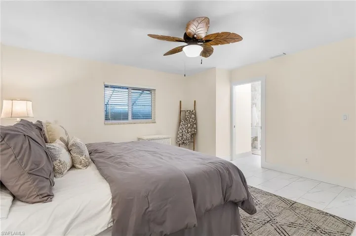 Bedroom featuring connected bathroom, ceiling fan, light tile flooring, and multiple windows