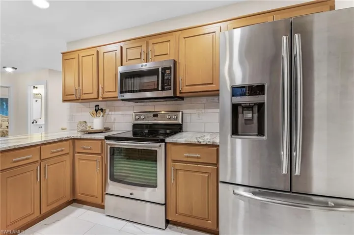 Kitchen with light tile flooring, light stone counters, tasteful backsplash, and appliances with stainless steel finishes