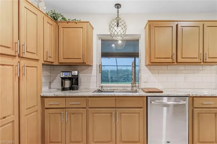 Kitchen with decorative light fixtures, backsplash, dishwasher, and light brown cabinetry