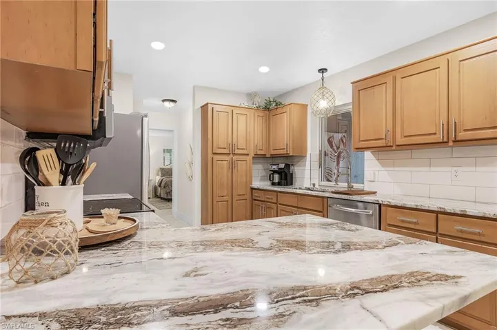 Kitchen with backsplash, light stone countertops, dishwasher, and decorative light fixtures