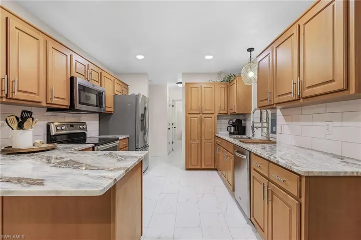 Kitchen featuring light tile flooring, tasteful backsplash, pendant lighting, and appliances with stainless steel finishes
