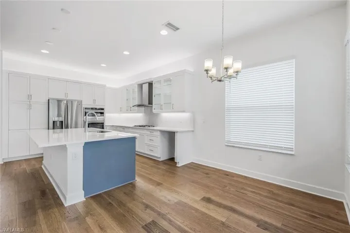Kitchen featuring appliances with stainless steel finishes, an island with sink, wall chimney exhaust hood, and dark hardwood / wood-style floors