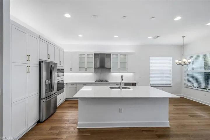 Kitchen with dark wood-type flooring, appliances with stainless steel finishes, an island with sink, and wall chimney exhaust hood