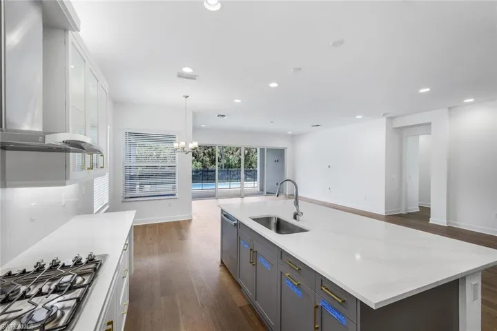 Kitchen featuring sink, wall chimney exhaust hood, a kitchen island with sink, and white cabinetry