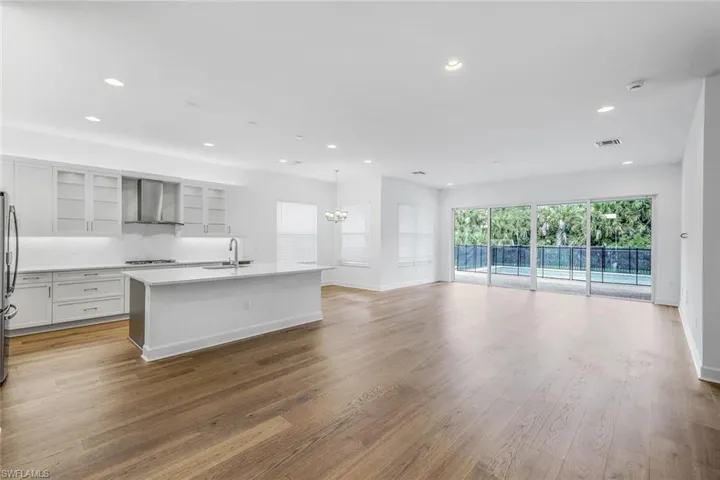Kitchen featuring an inviting chandelier, hardwood / wood-style flooring, wall chimney exhaust hood, an island with sink, and pendant lighting