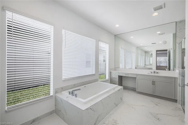 Bathroom with a healthy amount of sunlight, tile floors, tiled bath, and vanity