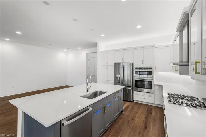 Kitchen featuring stainless steel appliances, an island with sink, white cabinets, dark hardwood / wood-style floors, and sink
