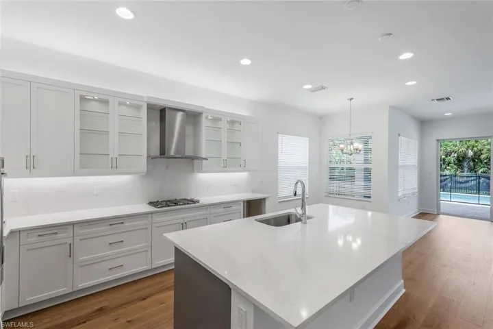 Kitchen featuring an island with sink, dark hardwood / wood-style flooring, pendant lighting, and wall chimney exhaust hood