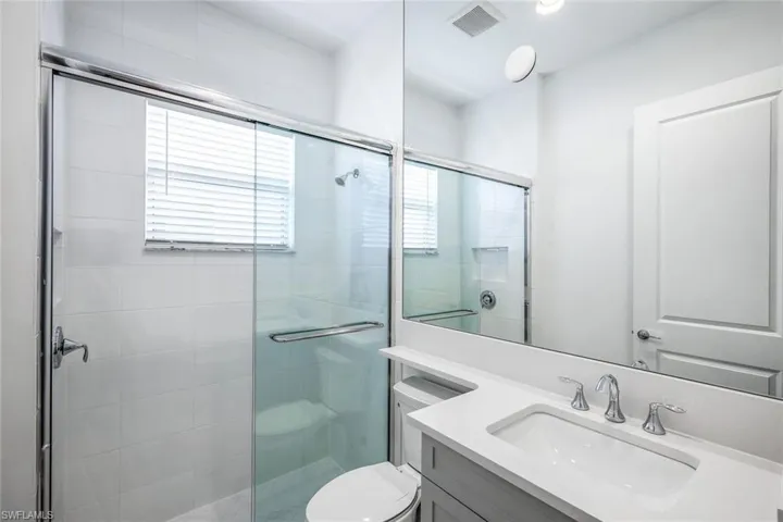 Bathroom featuring a shower with door, toilet, and vanity