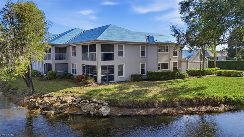Back of house with a water view, a yard, stucco siding, and a high end roof