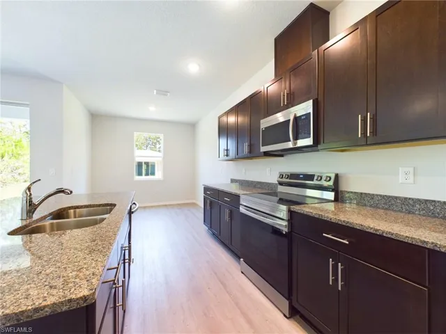 Kitchen with stainless steel appliances, light hardwood / wood-style floors, stone countertops, sink, and dark brown cabinets