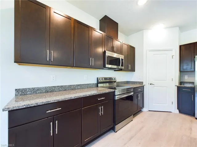Kitchen with light wood-type flooring, light stone countertops, appliances with stainless steel finishes, and dark brown cabinetry